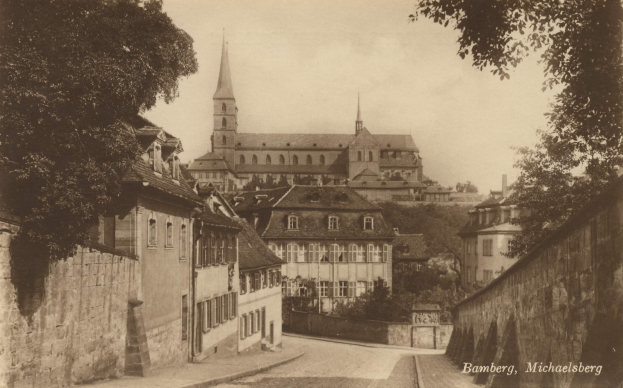 Altes Schwarz-Weiß-Foto einer Stadtstraße mit einer Kirche im Hintergrund, Mauern auf beiden Seiten, Bäume säumen die Straße und der Himmel ist oben sichtbar; die Kirche befindet sich in Bamberg, Deutschland.