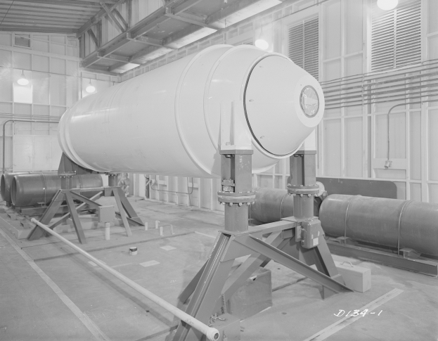 Großer zylindrischer Wasserstoffbomben auf einem Ständer in einer industriellen Fabrikumgebung mit Rohren, Lampen und einer Wand im Hintergrund.