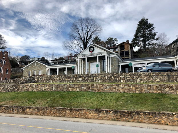 Steinwand mit parkenden Autos, benachbarten Gebäuden mit Fenstern und Türen, Bäumen und einem bewölkten Himmel, als das kürzlich wiedereröffnete Weltkulturerbe-Museum bezeichnet.