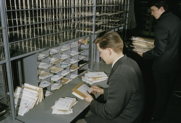 Zwei Männer in Anzügen, die Dokumente an einem Tisch in einem Rechenzentrum mit Aktenschränken im Hintergrund überprüfen.