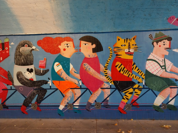 Mural an einer Gebäudeseite, das Menschen beim Radfahren zeigt, mit einer Straße darunter und Himmel darüber, Teil einer Londoner Street-Art-Serie.