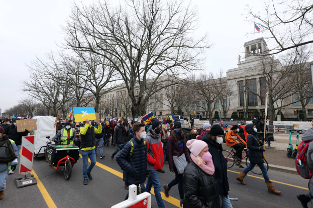 Eine große Gruppe von Menschen marschiert in Washington, D.C. am 21. Januar 2020 mit Plakaten und Bannern, einige fahren Fahrräder, mit Bäumen und einem Gebäude im Hintergrund bei klarem blauem Himmel.