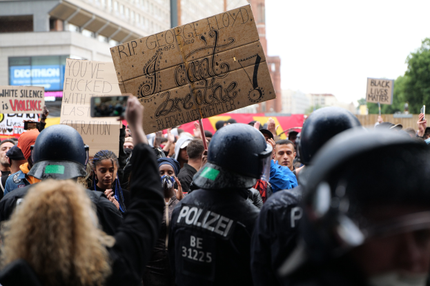Gruppe von Menschen mit Helmen, die Schilder und Mobiltelefone halten, vor einem Gebäude, Bäumen und einem Pfahl