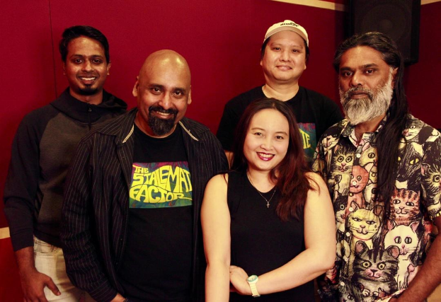 Eine Gruppe von Menschen, die zusammen in einem Aufnahmestudio posen, lächeln und bequem gekleidet sind, mit ihren Armen umeinander gelegt.